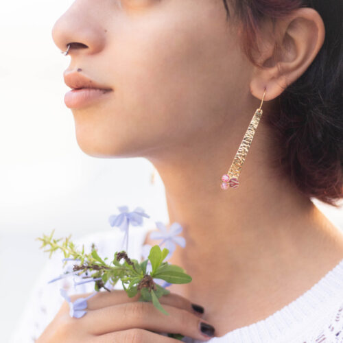 Visage d'une femme portant une boucle d'oreille pendante en or avec une pierre semi-précieuse rose