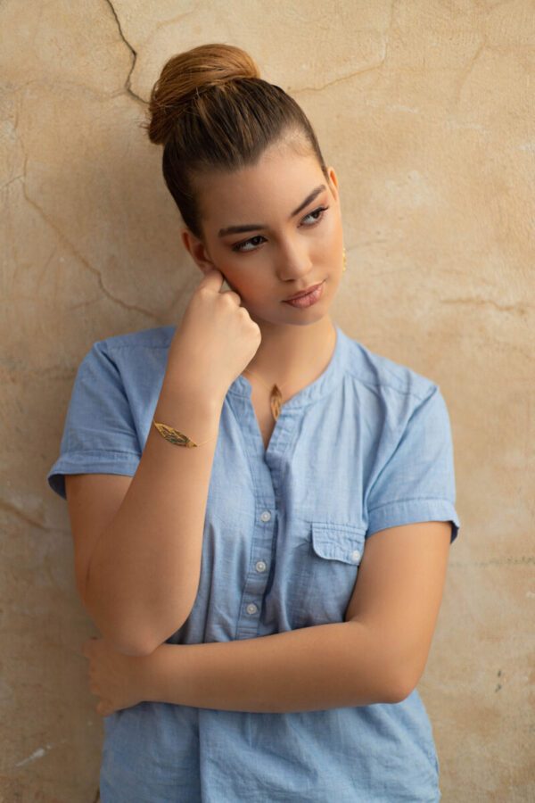 Femme appuyée contre un mur et portant un bracelet fin avec design de feuille en or